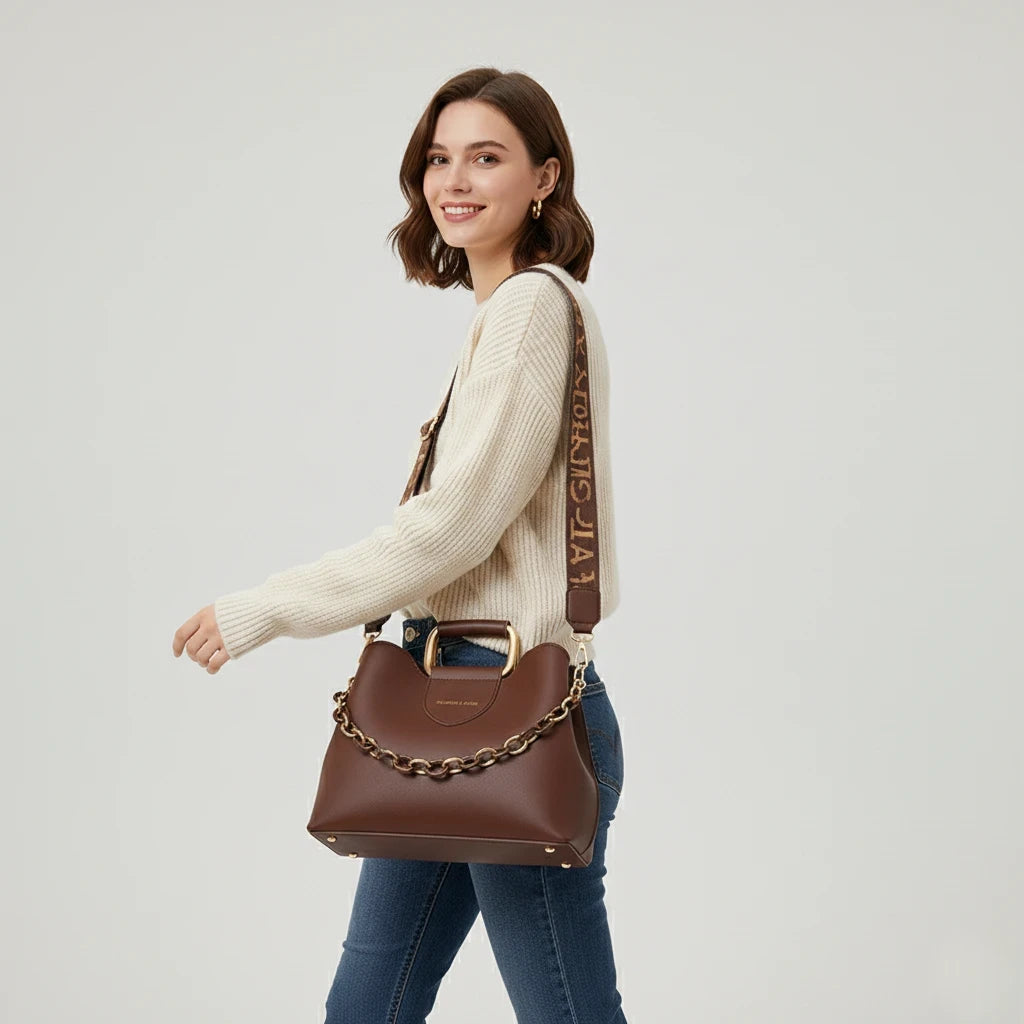 Woman holding a brown handbag with a chain detail on a light gray background