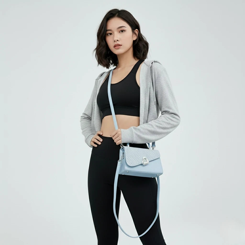 Woman in athletic wear holding a light blue handbag against a plain background