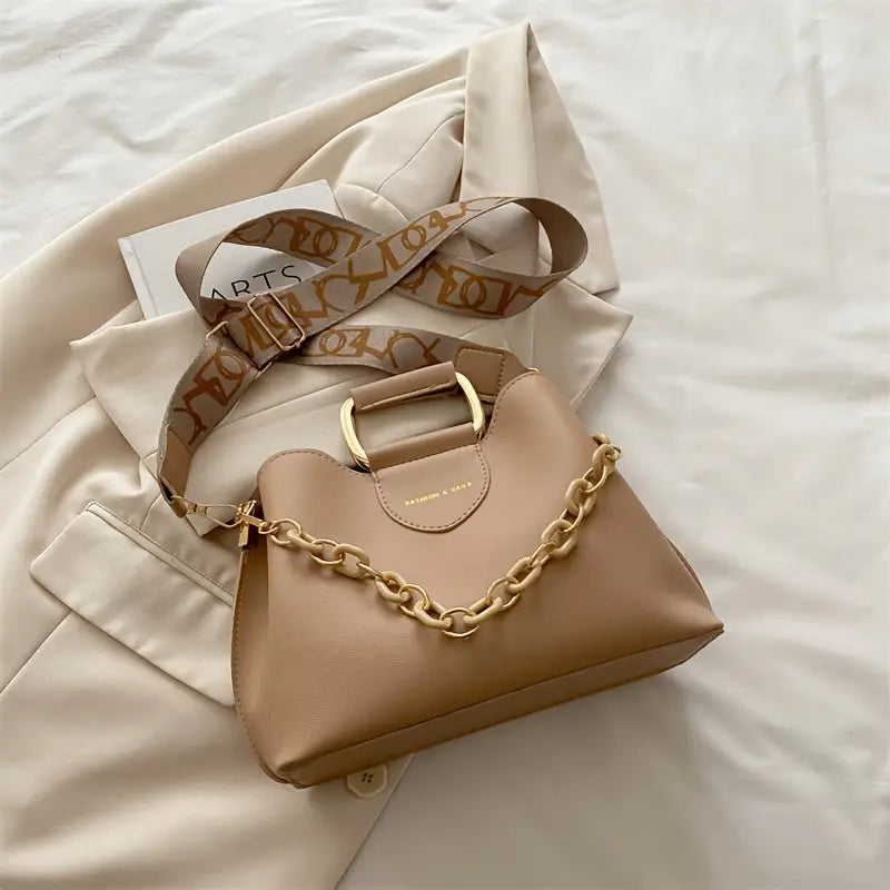 Beige handbag with gold chain detail on a light beige fabric background