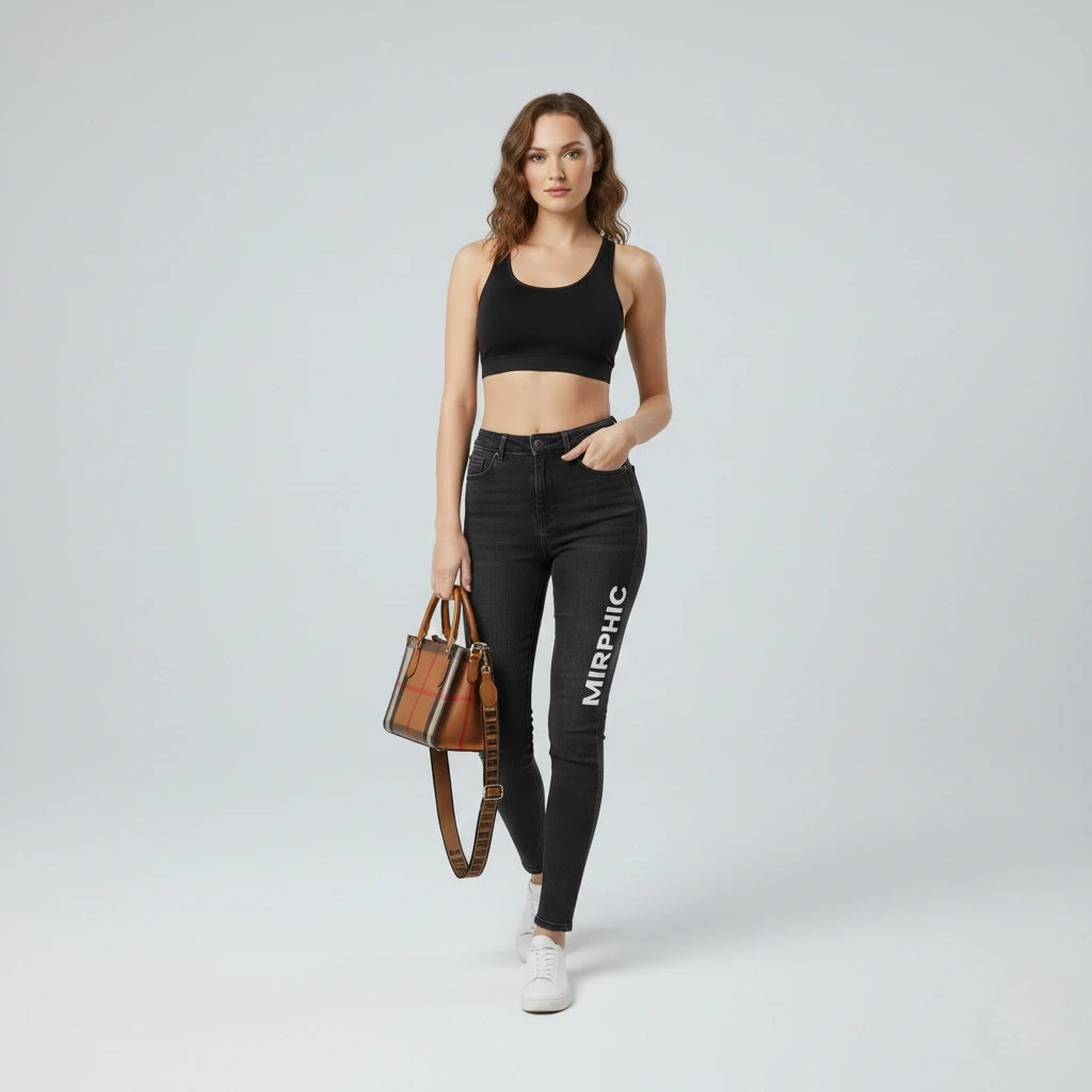Woman wearing black jeans with 'MIRPHIC' branding, holding a brown handbag on a white background