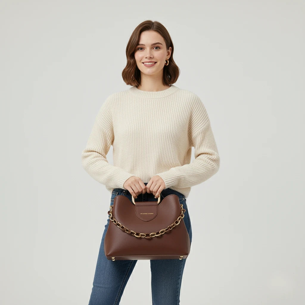 Woman holding a brown handbag with a chain detail against a plain background