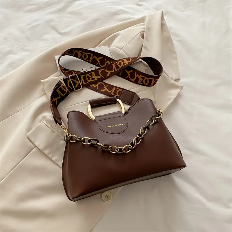 Brown handbag with gold chain detail on a beige fabric background
