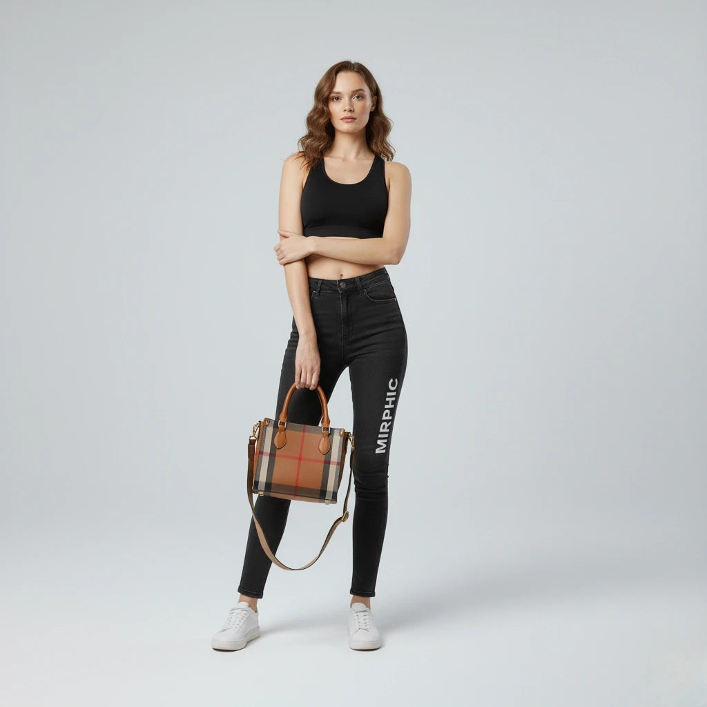 Woman wearing black jeans with 'MIRPHC' branding, holding a plaid handbag on a light gray background