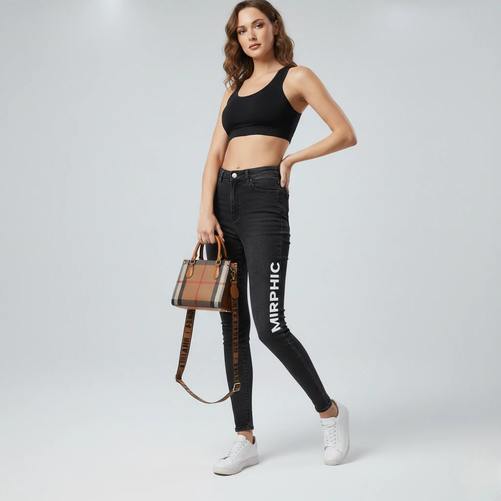 Woman wearing black jeans with 'MIRPHIC' branding, holding a checkered handbag on a light gray background