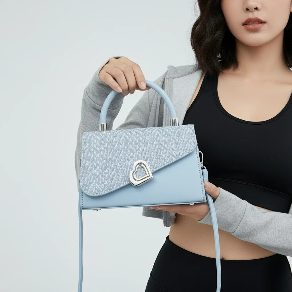 Woman holding a light blue handbag with a heart-shaped clasp against a plain background