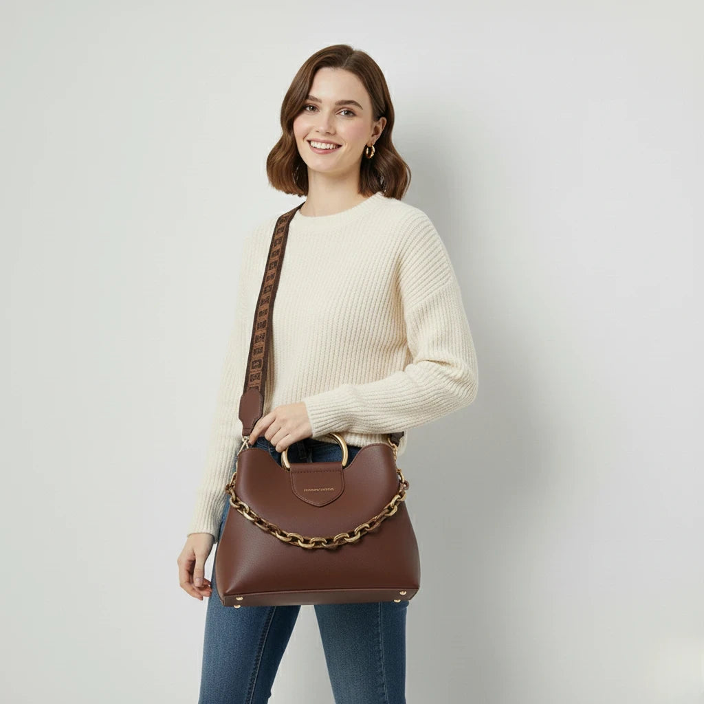 Woman holding a brown handbag with a gold chain detail against a plain background
