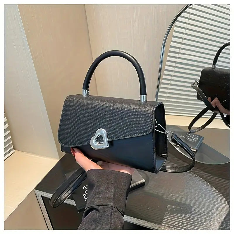 Black handbag with a silver clasp held by a person on a reflective surface.