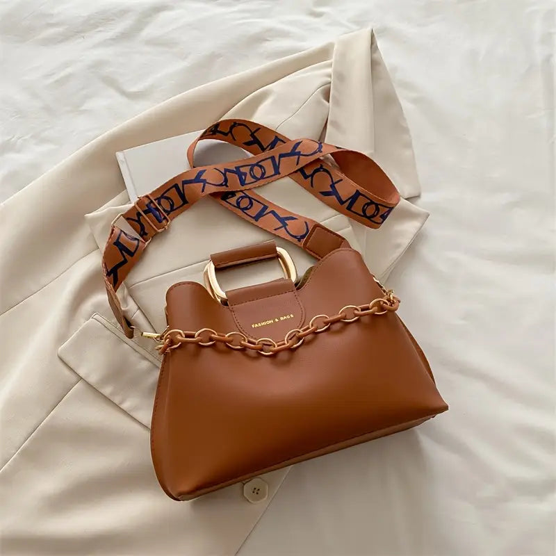 Brown handbag with a patterned strap on a light beige fabric background