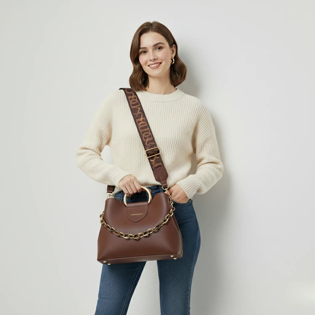 Woman holding a brown handbag with gold chain detail against a plain background