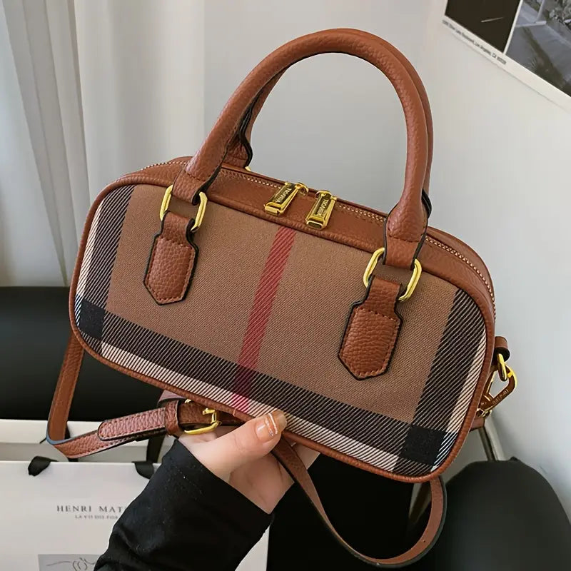 Brown checkered handbag with gold accents held by a person indoors.