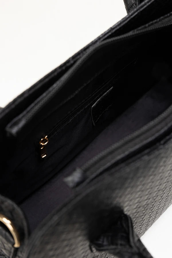 Close-up of a black textured handbag with gold accents on a white background