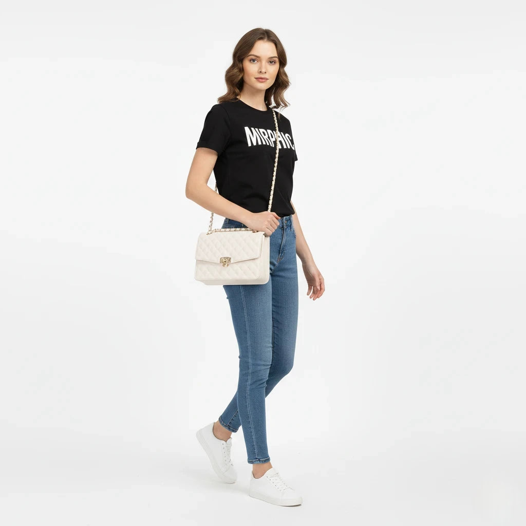 Woman wearing a black t-shirt with text, blue jeans, and white sneakers, holding a beige handbag on a white background.