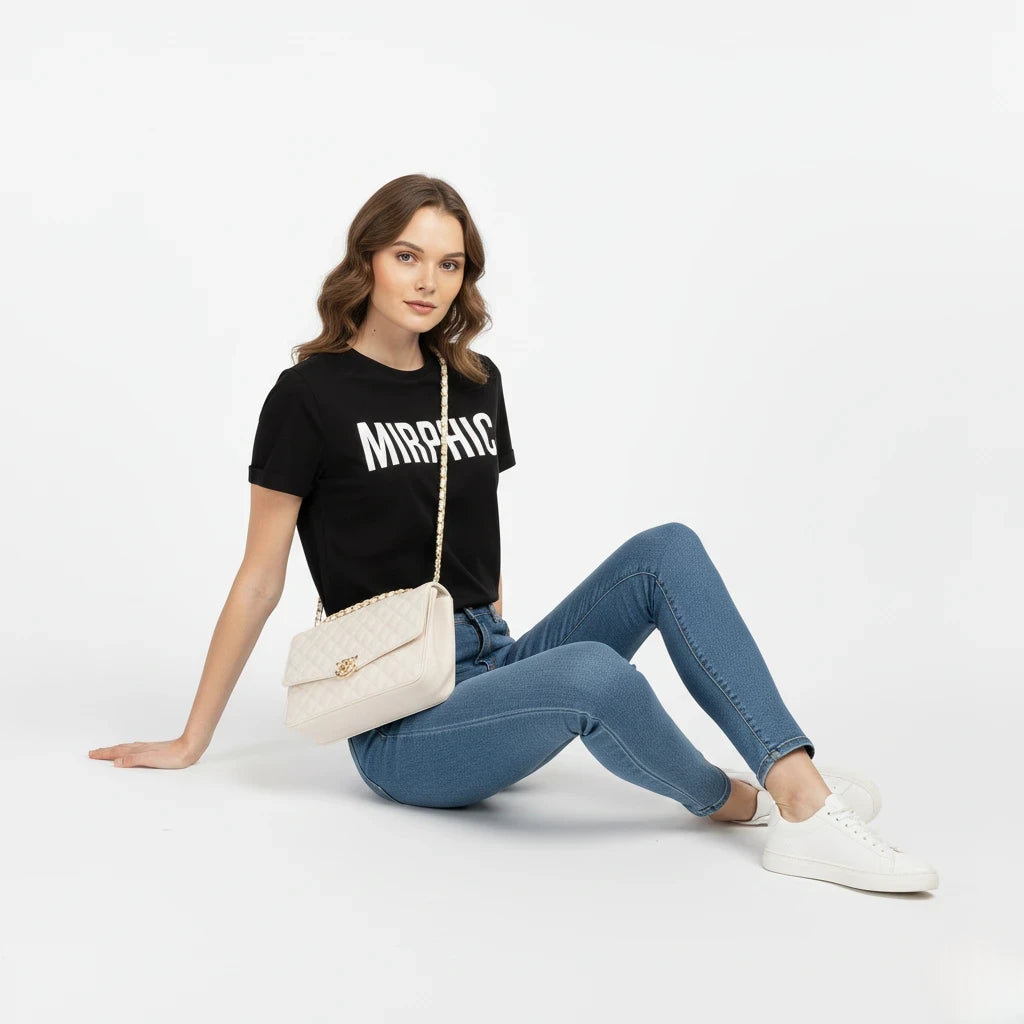 Woman wearing a black t-shirt with 'MIRPIC' text, blue jeans, and white sneakers, sitting on the floor with a beige handbag.