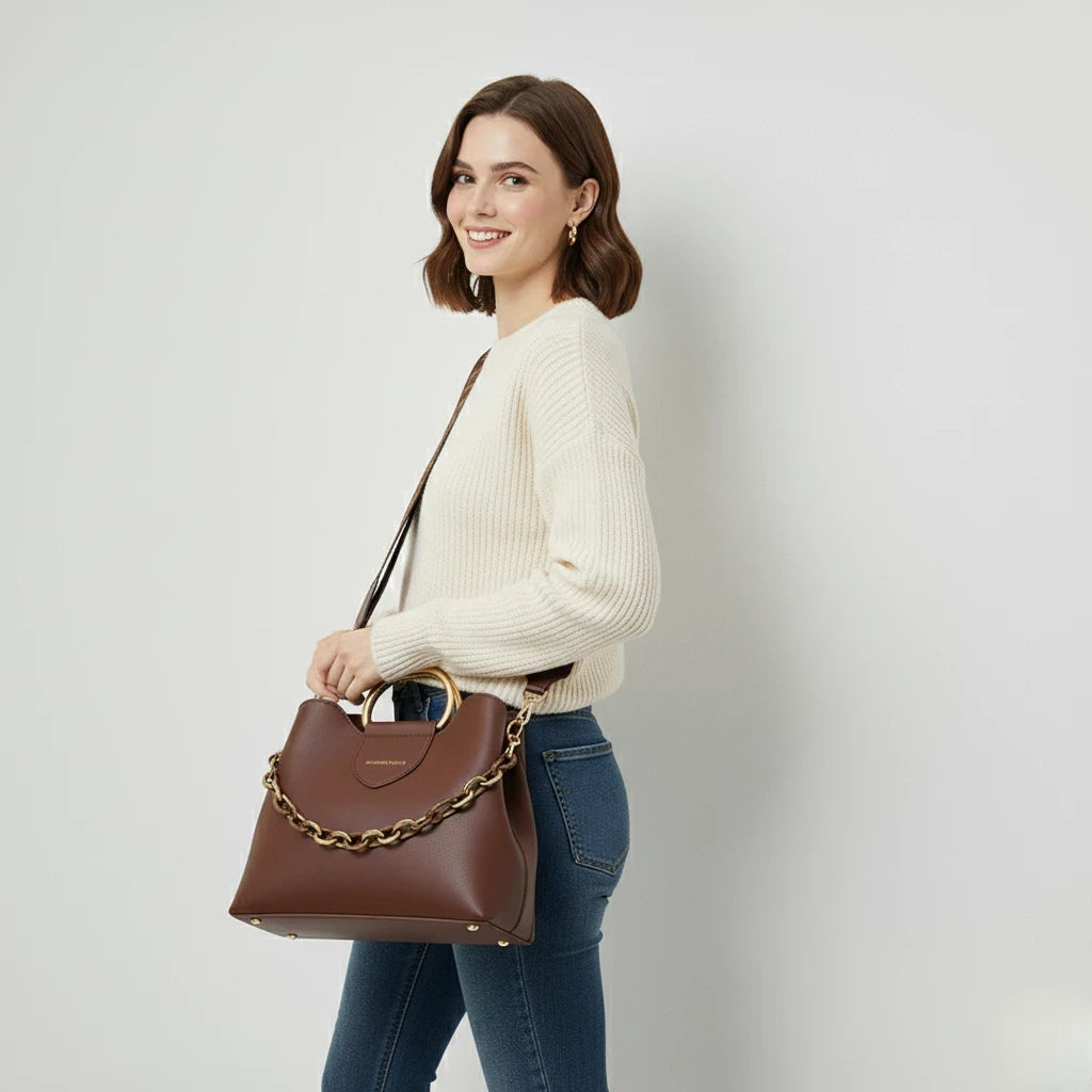 Woman holding a brown handbag with a chain detail against a plain background