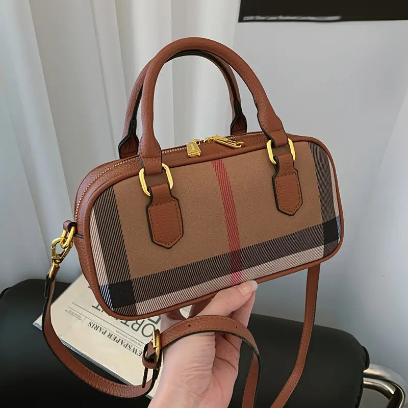 Brown checkered handbag with gold accents held by a hand against a neutral background
