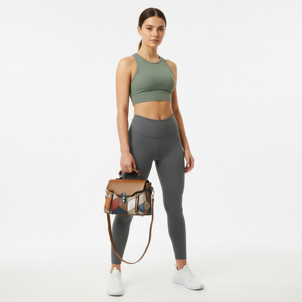 Woman wearing a green sports bra and gray leggings holding a multicolored handbag on a white background