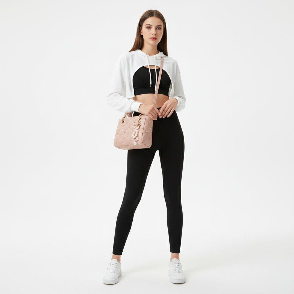 Woman wearing a white hoodie, black crop top, and leggings holding a pink handbag on a white background