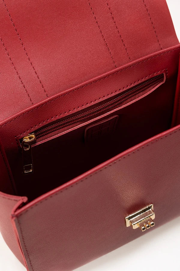 Close-up of a red handbag with a gold zipper and clasp on a white background