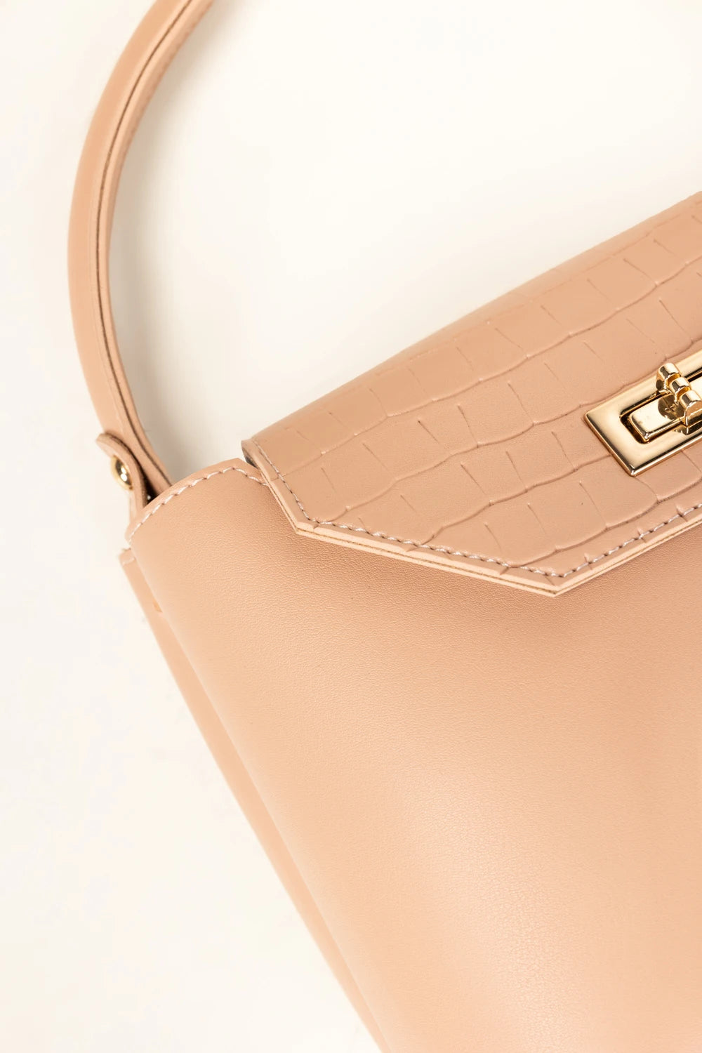 Close-up of a beige handbag with a gold clasp on a light background