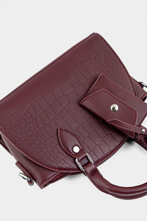 Maroon handbag with textured surface and silver hardware on a light gray background