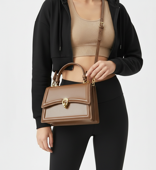 Person holding a brown handbag with a gold clasp on a light gray background