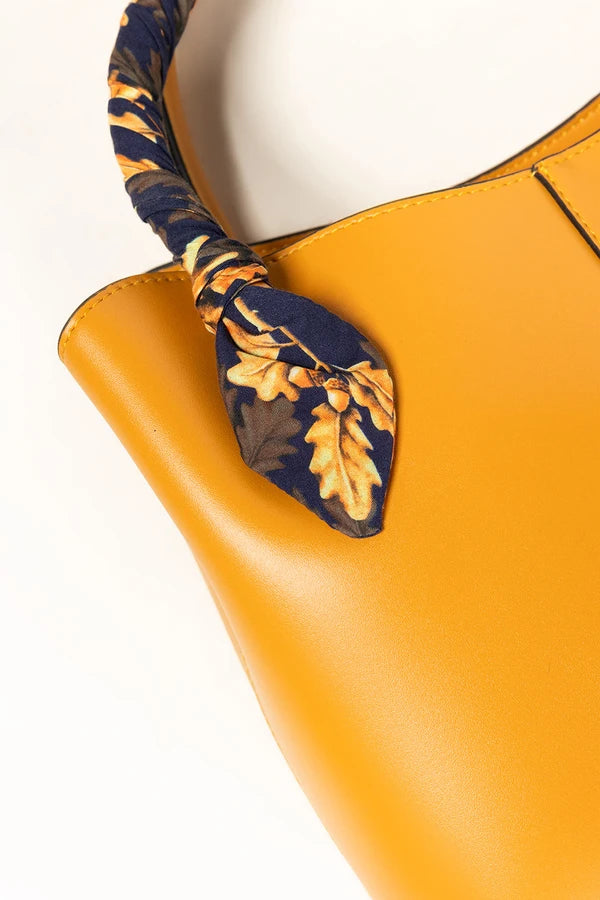 Yellow handbag with a decorative leaf-patterned handle on a white background